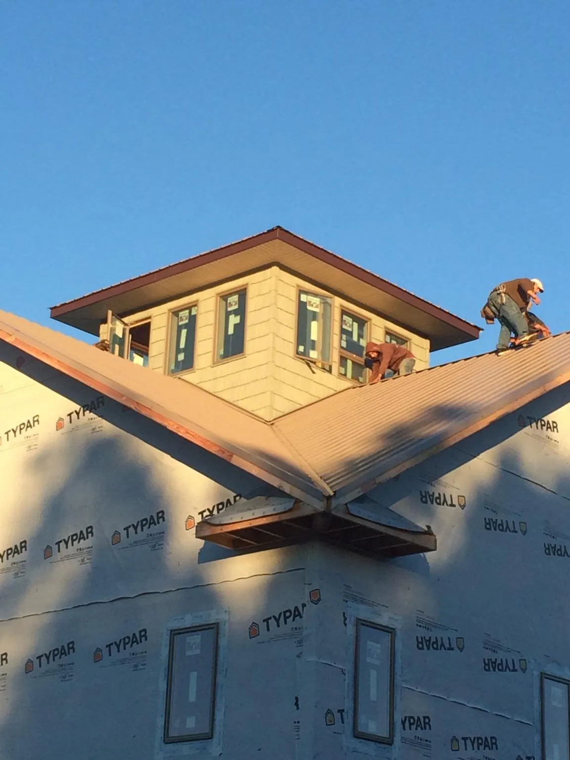 Roofers working around a rooftop cupola on a new metal roof at sunset — Roof Waterproofing in Bethel by Roofing Brothers